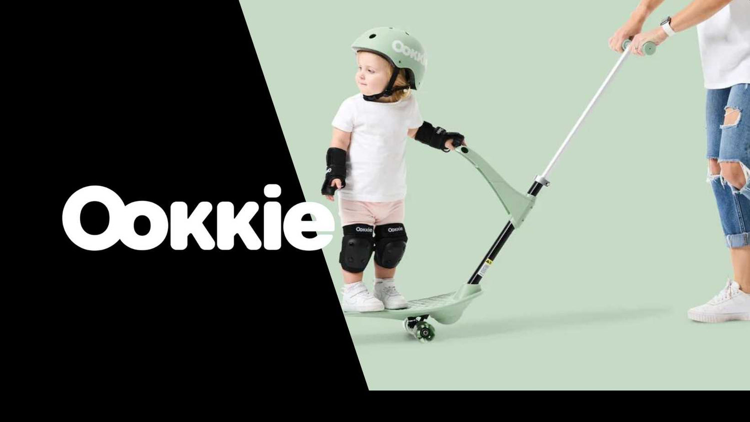 Toddler riding Ookkie scooter with safety gear and handle assist.