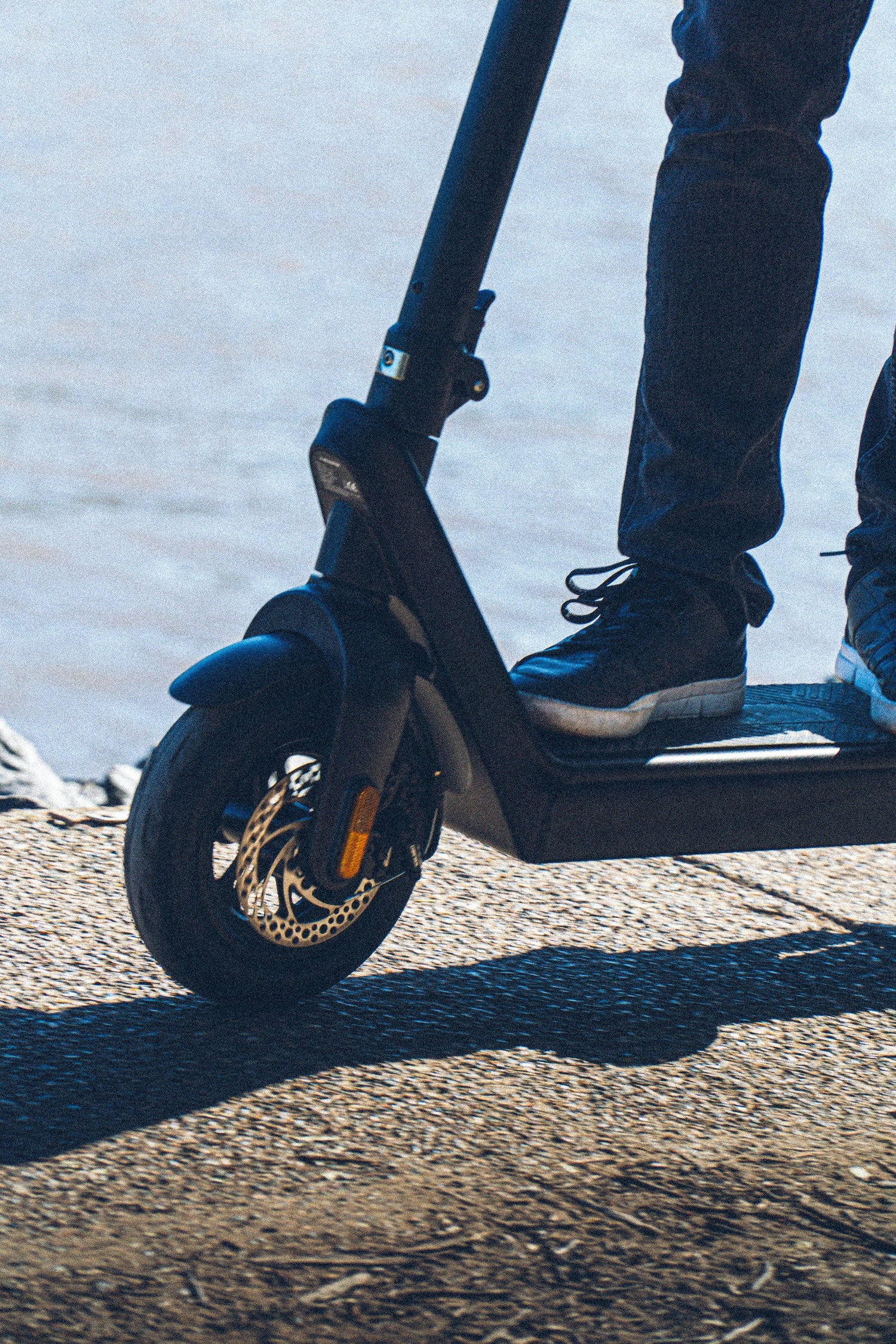 Close-up of person riding electric scooter near waterfront.
