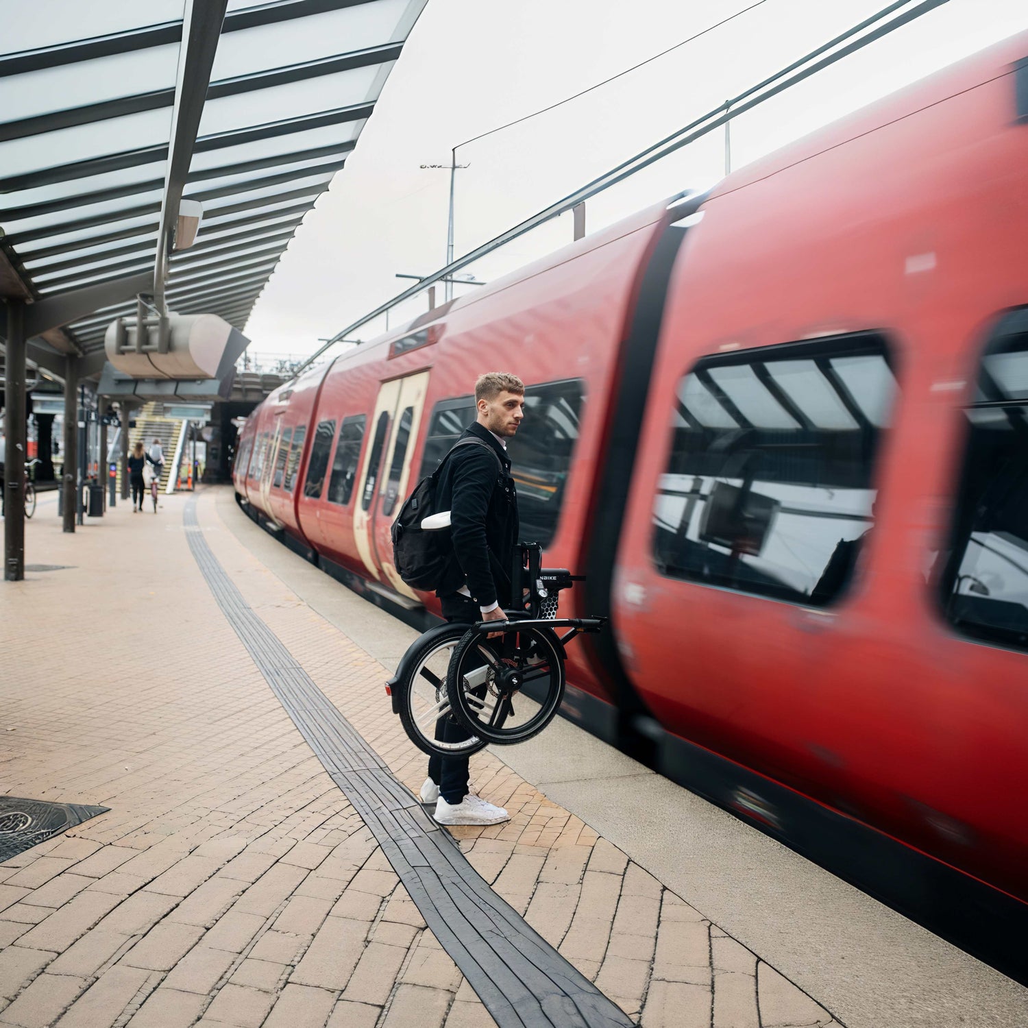 Man carrying folded electric bike at train station platform.