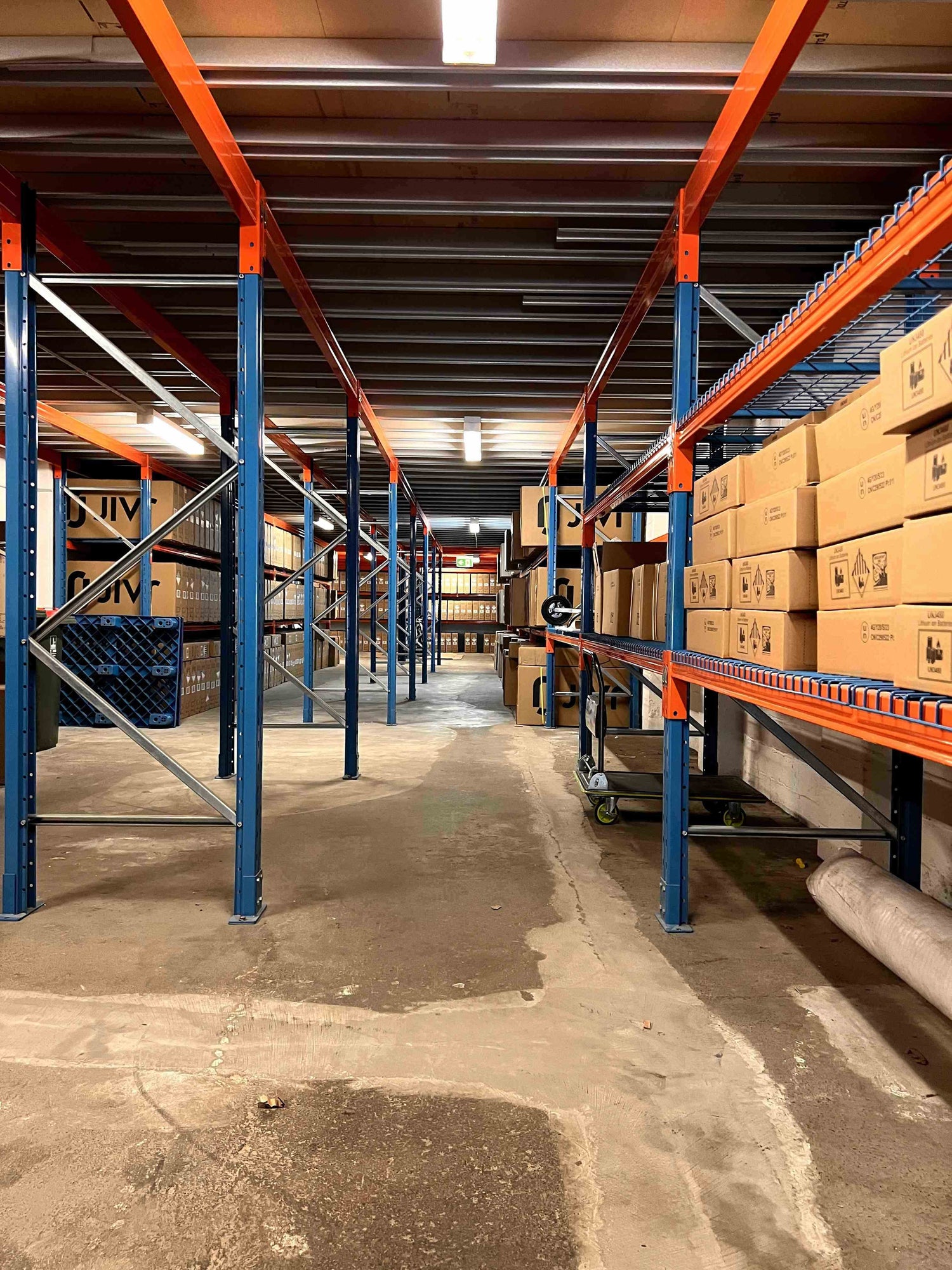 Warehouse aisle with shelving and stacked cardboard shipping boxes.