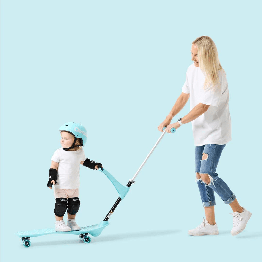 Mother pushing toddler on aqua blue scooter with safety gear.