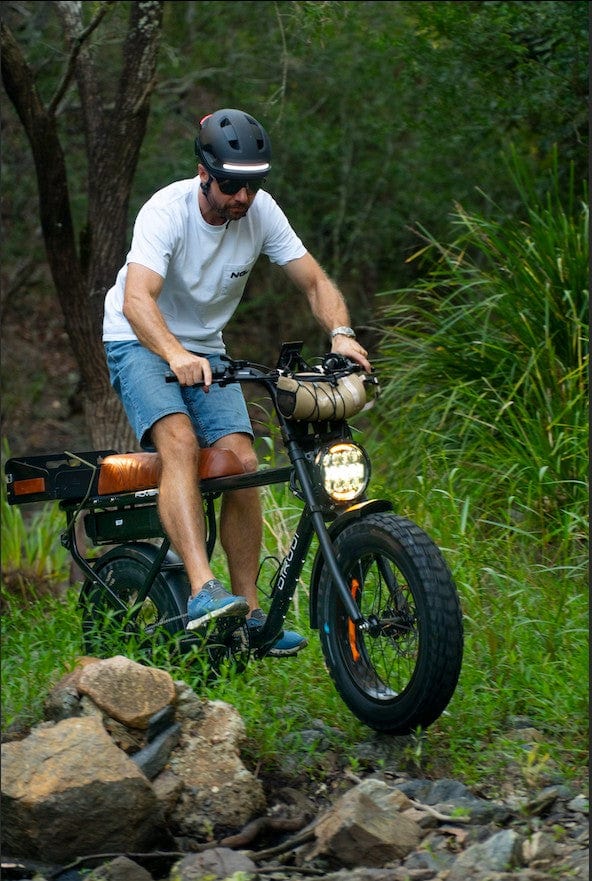 Man riding electric bike off-road through rocky forest trail.