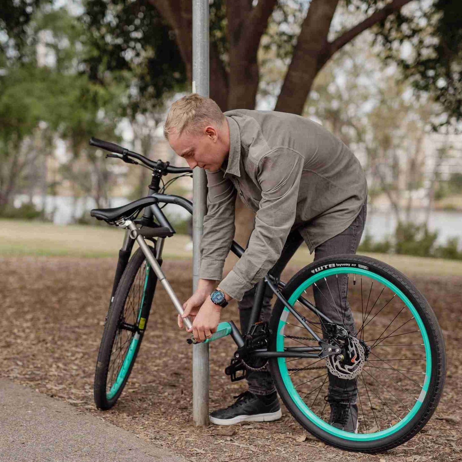 Man locking bicycle to pole in park using U-lock