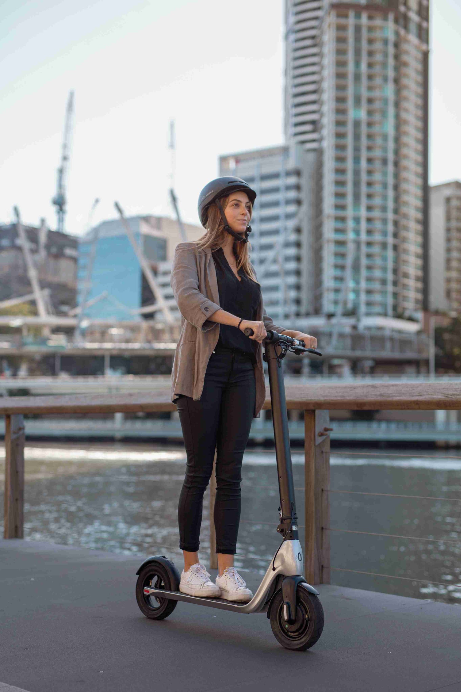 Woman wearing helmet riding electric scooter by city waterfront