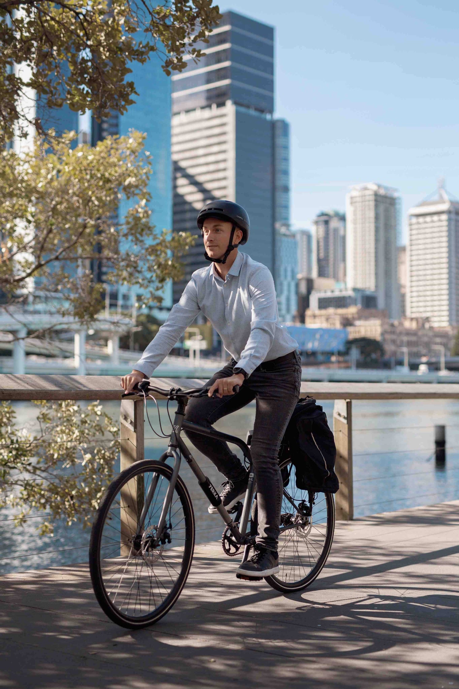 Man wearing helmet riding bicycle along waterfront in cityscape background