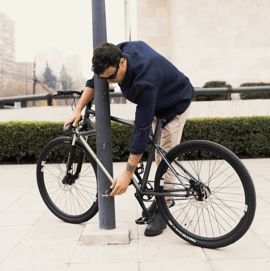 Man securing bicycle to pole with lock in urban setting