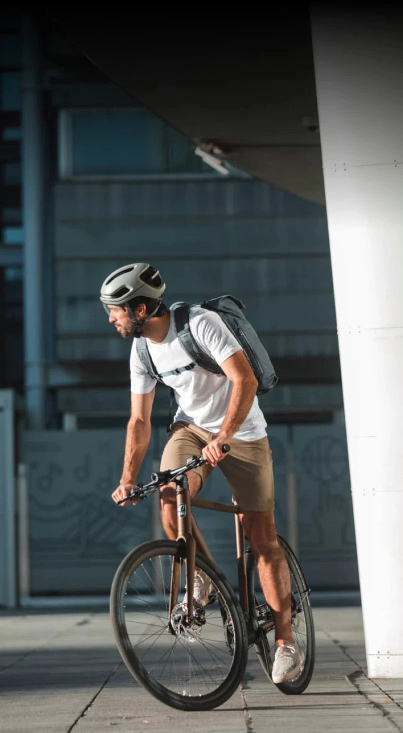 Man cycling in city wearing smart helmet and backpack.