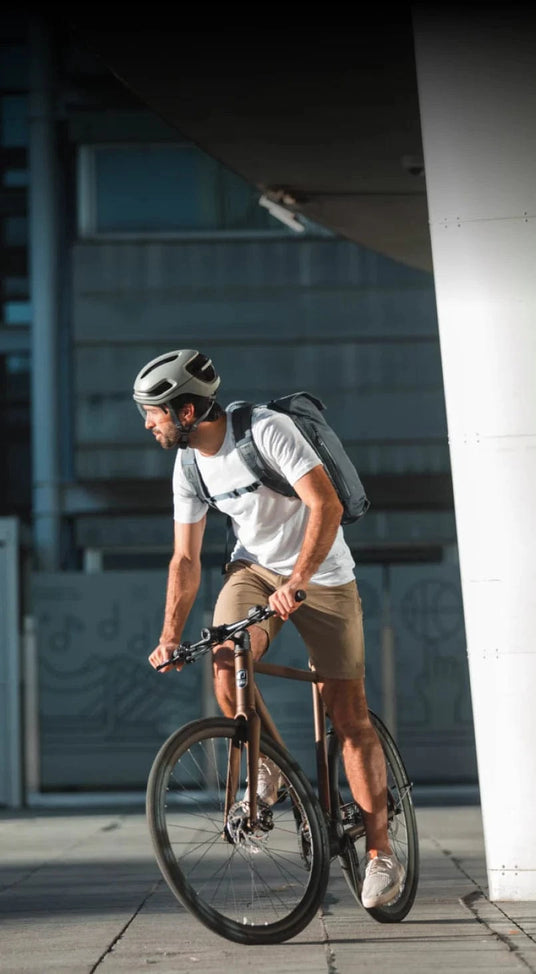 Man cycling in city wearing smart helmet and backpack.