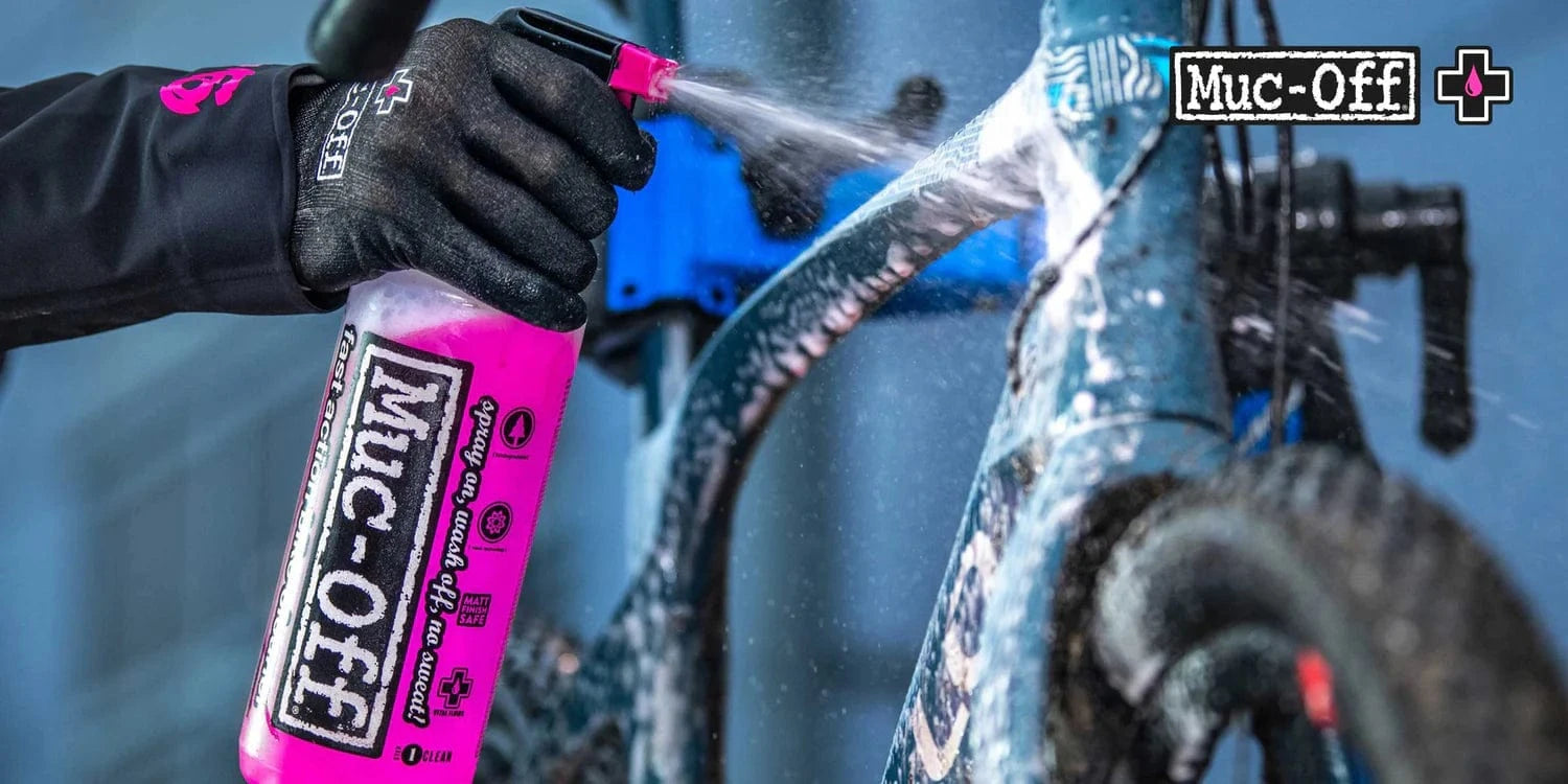 Person spraying Muc-Off cleaner onto dirty mountain bike frame.