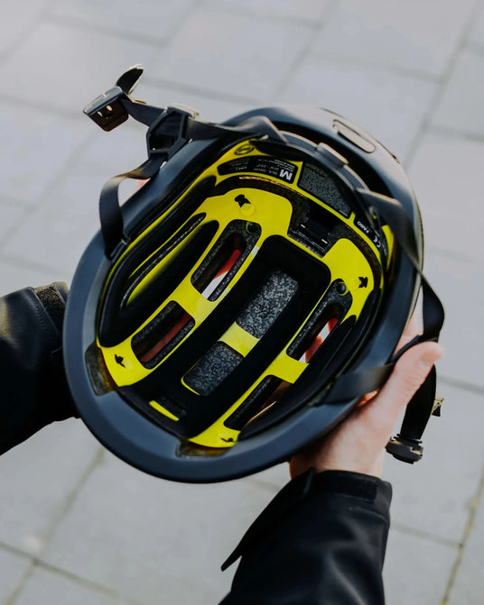 Close-up of hands holding helmet showing yellow MIPS liner.